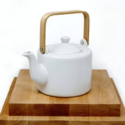 matte white teapot with wood handle and lid closed, on top of wood cutting boards