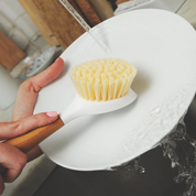 Caucasian person scraping dish with back end of dish brush under running water by full circle