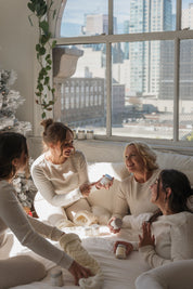Four women in a cozy room with a cityscape view, one holding a phone.