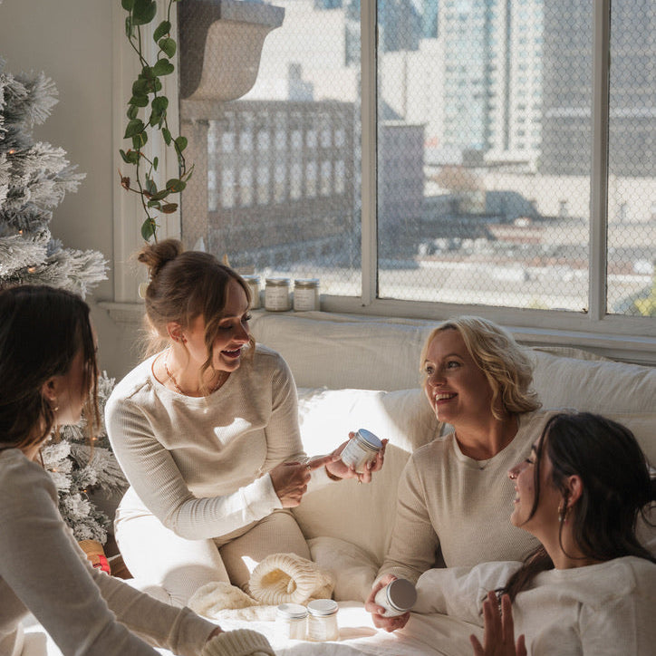 Four women in a cozy room with a cityscape view, one holding a phone.