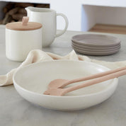 White ceramic bowl with wooden utensils on a marble countertop, with kitchen items in the background.
