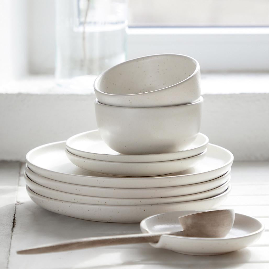 Set of white ceramic dishes on a light surface with a blurred window background