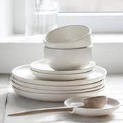 Set of white ceramic dishes on a light surface with a blurred window background