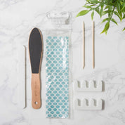 Pedicure tool set with a file, pedicure brush, and packaging on a marble surface.