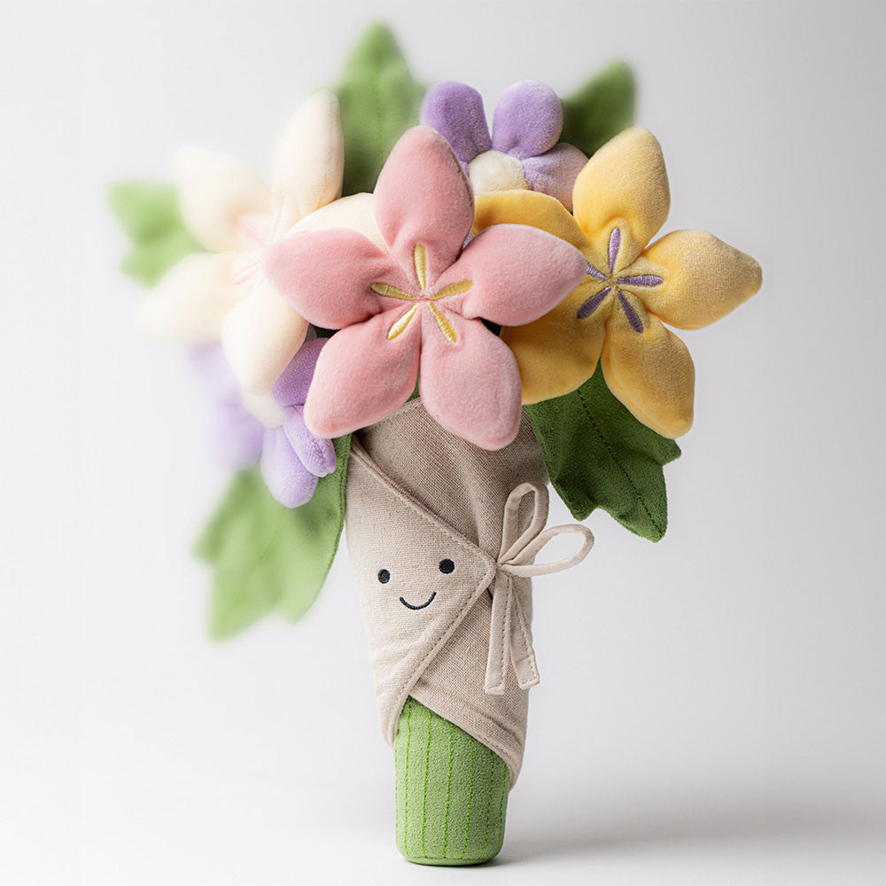 Plush jellycat  bouquet of pink purple white and yellow flowers with a smiling face on a beige background