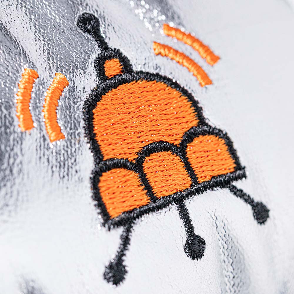detail close up of orange spaceship shaped jellycat logo stitched on silver fabric