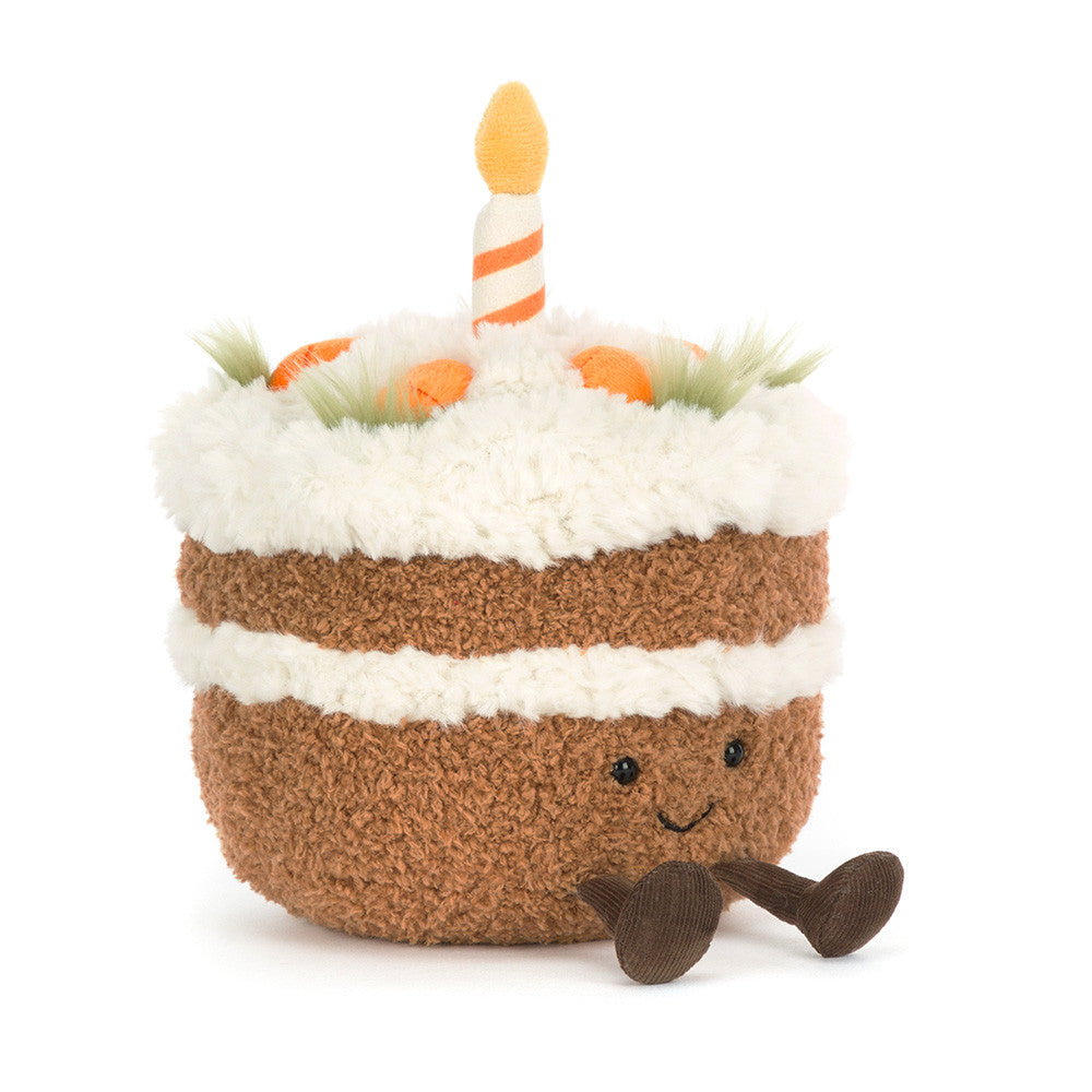 Plush toy carrot cake with smiling face, little feet and with candles on a white background