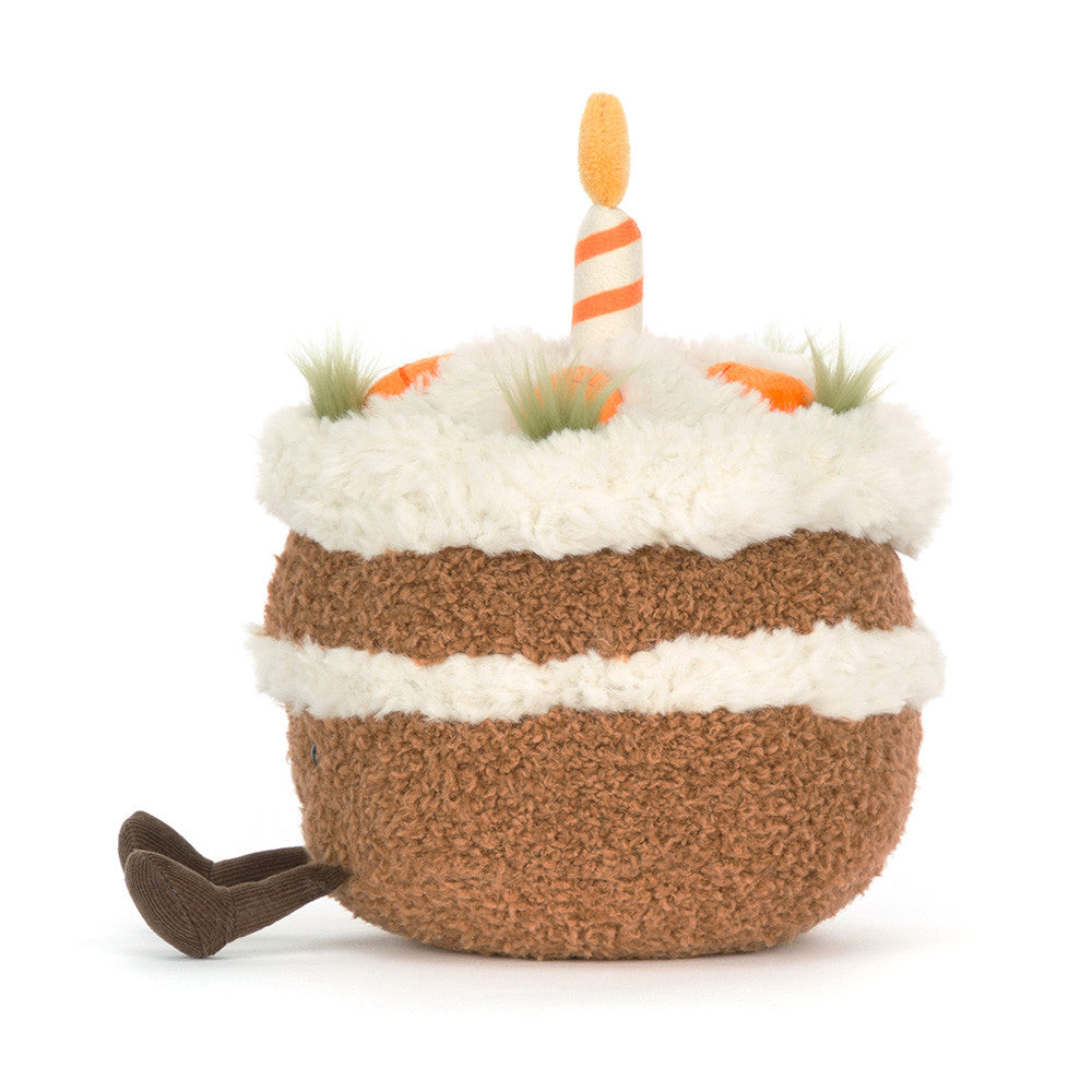 Plush toy carrot cake with smiling face, little feet and with candles on a white background