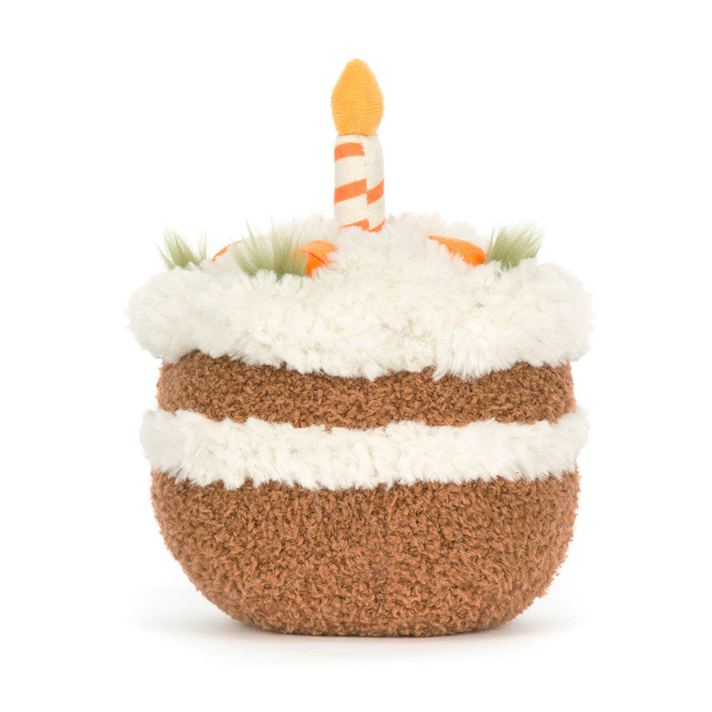 Plush toy carrot cake with smiling face, little feet and with candles on a white background