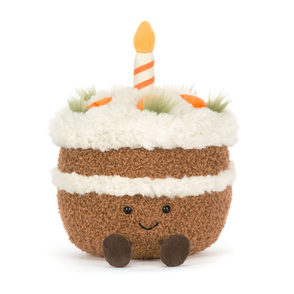 Plush toy carrot cake with smiling face, little feet and with candles on a white background