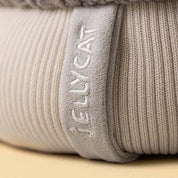 close up of A plush toy toque by jellycat with a gray cable-knit top, a cream ribbed bottom, a gray pom-pom, and small fabric hands and feet