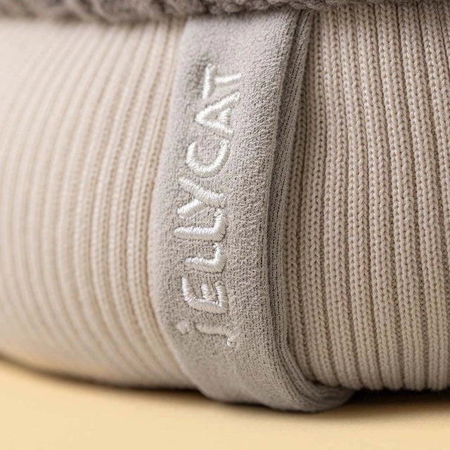 close up of A plush toy toque by jellycat with a gray cable-knit top, a cream ribbed bottom, a gray pom-pom, and small fabric hands and feet
