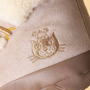 close up of A plush boot-shaped jellycat brand plush toy with a cream sherpa upper, beige corduroy-like lower section, and a tan hanging loop at the top, shown on a plain white background.