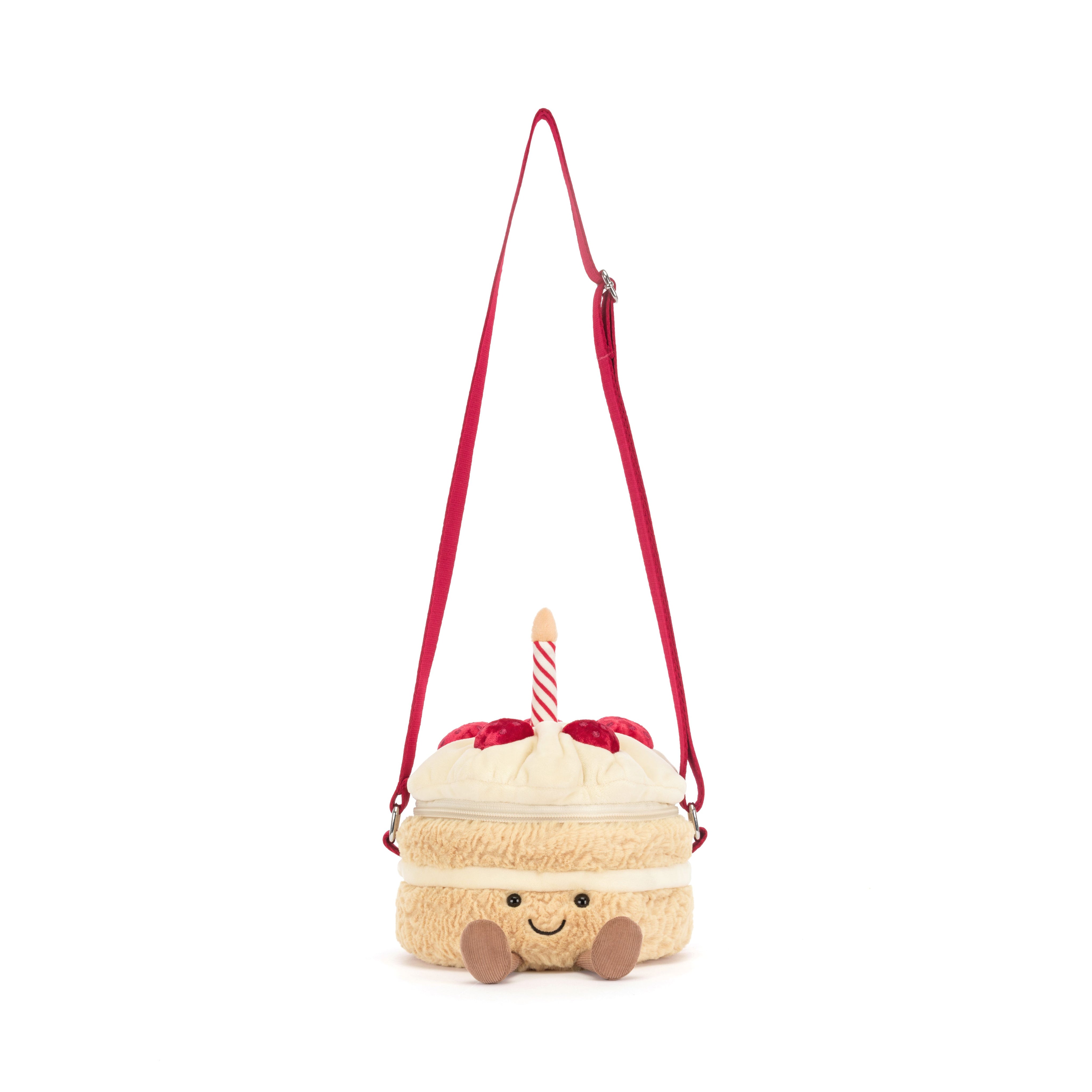 A plush crossbody bag shaped like a cute cream-colored cake with red strawberries and a red and white stripe candle, featuring a red shoulder strap and a smiling face on a white background.