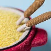 close up of Red jellycat plush fondue pot with a face, cheese inside, and wooden forks sticking out on a white background