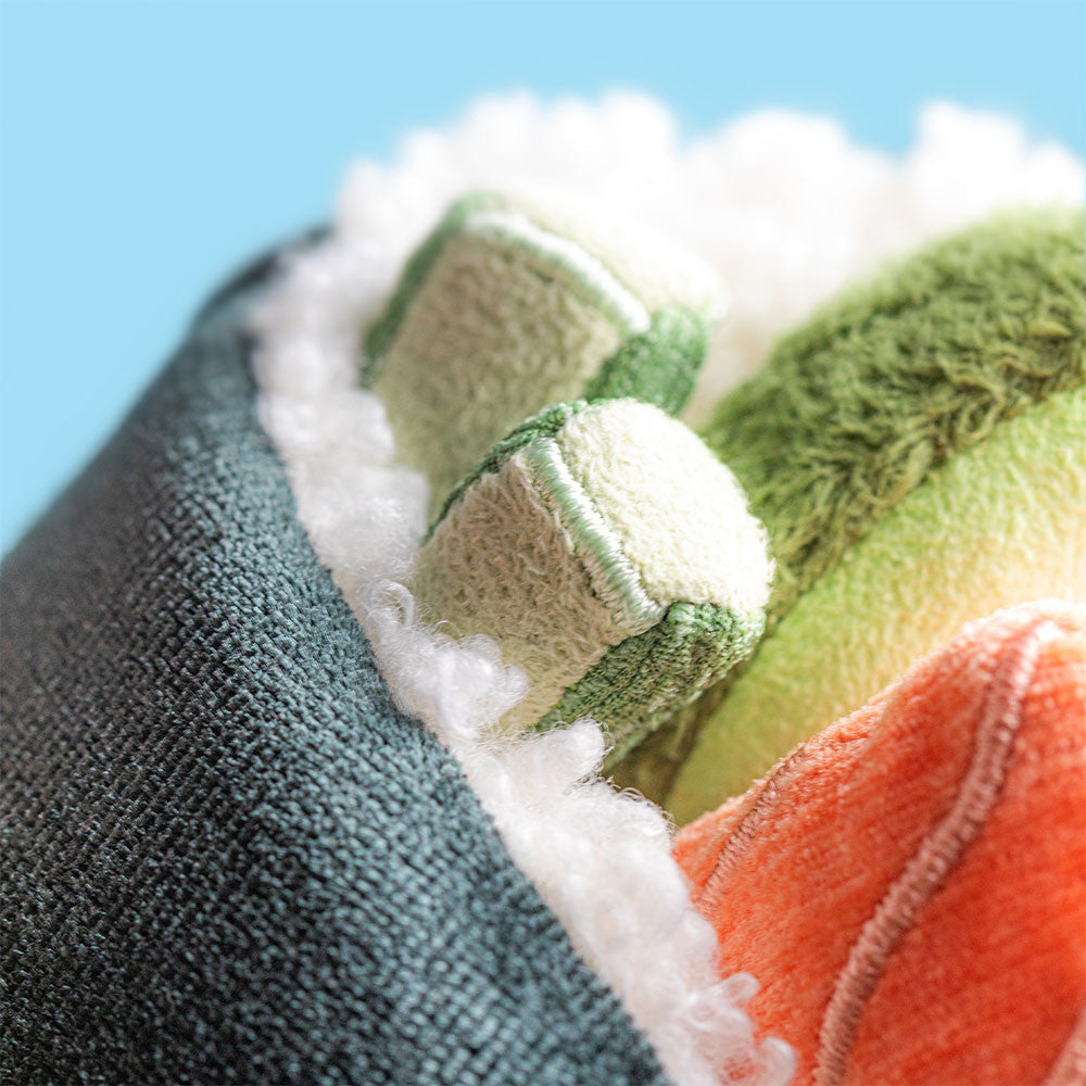 close up of Plush jellycat toy shaped like a sushi roll with black exterior, pink and green fillings on a white background
