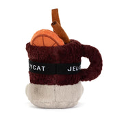 back view of A jellycat brand plush toy shaped like a  mug of mulled spiced drink with a smiling face, wearing orange ski goggles and brown boots, on a solid white background.