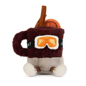 A jellycat brand plush toy shaped like a  mug of mulled spiced drink with a smiling face, wearing orange ski goggles and brown boots, on a solid white background.