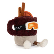 A jellycat brand plush toy shaped like a  mug of mulled spiced drink with a smiling face, wearing orange ski goggles and brown boots, on a solid white background.