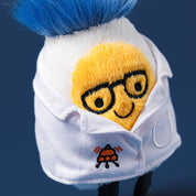 detail shot of smiling boiled egg plush toy with black rim glasses, blue hair and white scientist lab coat on blue background 