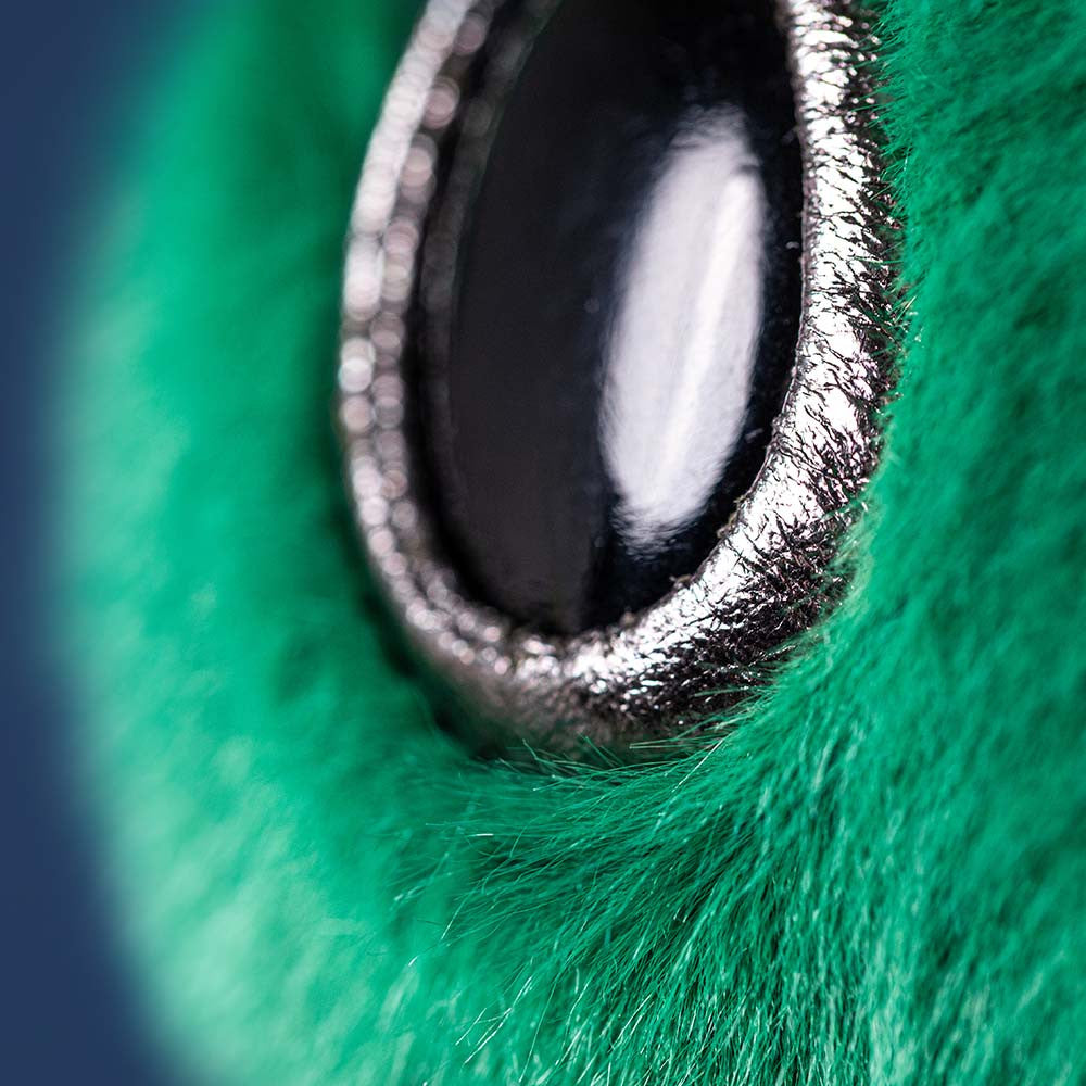 close up detail of shiny black toy eye of alien with green fur face