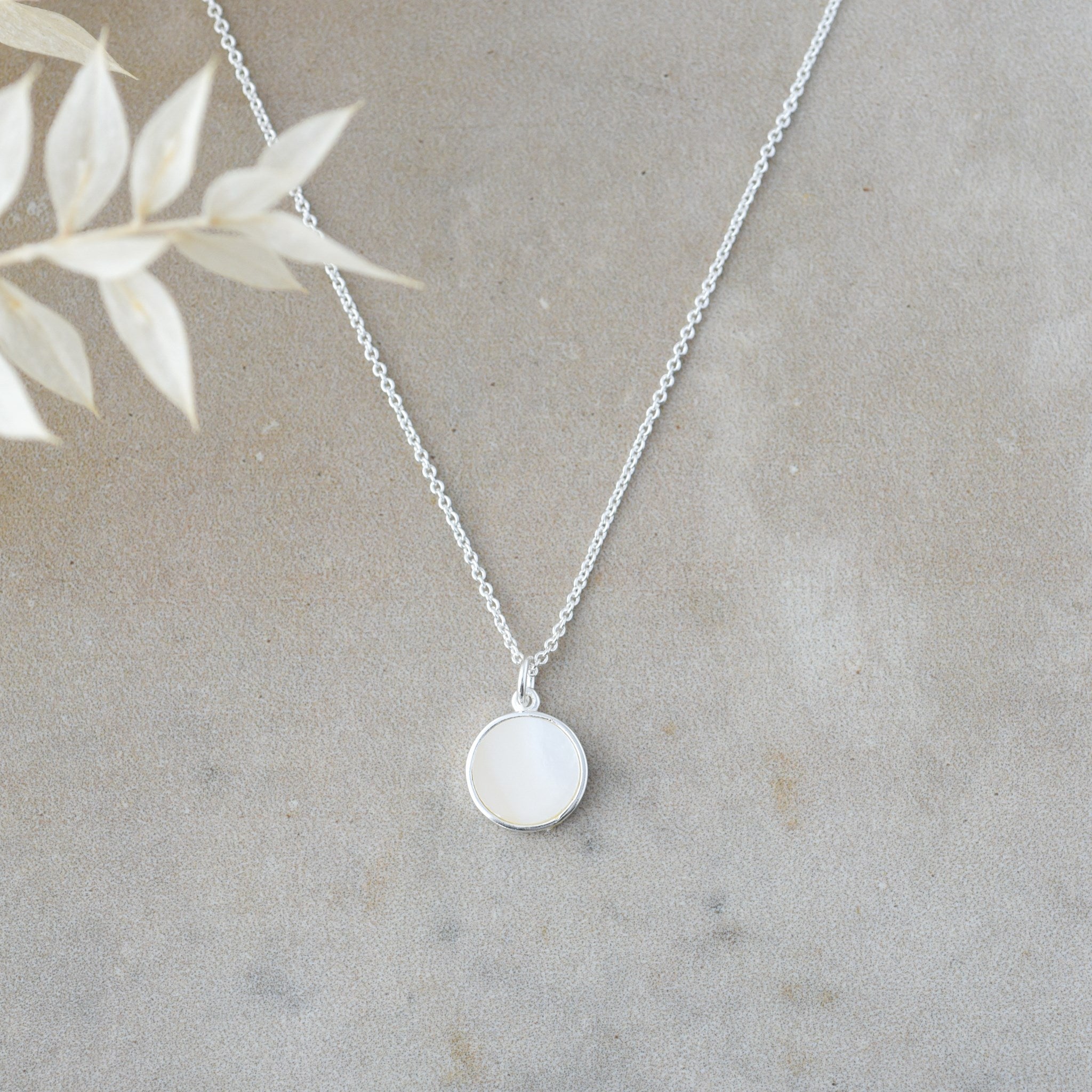 Silver necklace with a round pendant on a neutral background