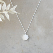 Silver necklace with a round pendant on a neutral background