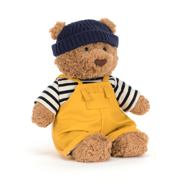 jellycat bartholomew Teddy bear dressed as a sailor wearing a navy hat, striped shirt, and yellow overalls on a white background