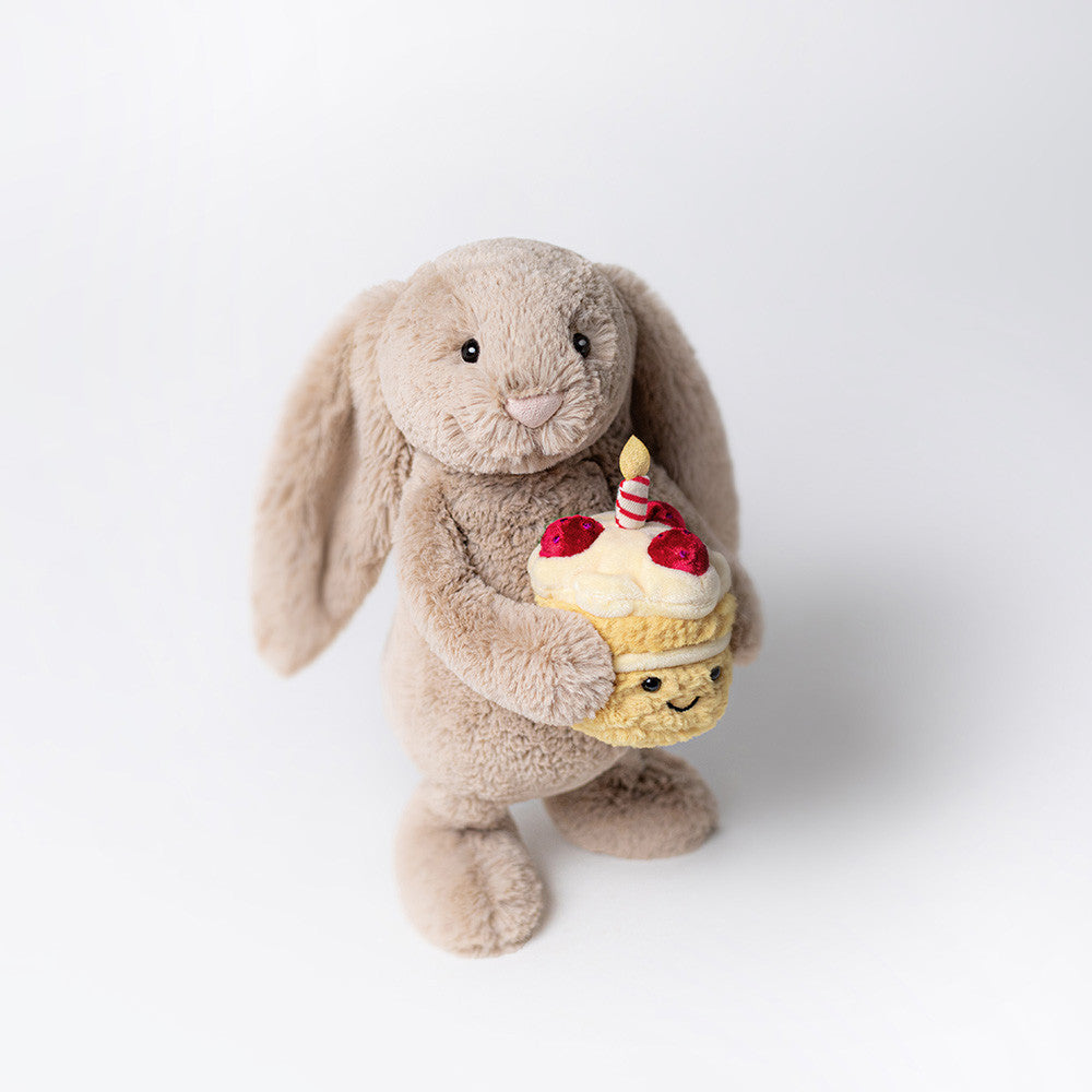 Plush jellycat bunny holding a birthday cake with a candle on a white background