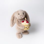 Plush jellycat bunny holding a birthday cake with a candle on a white background