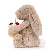 side view of a Plush jellycat bunny holding a birthday cake with a candle on a white background
