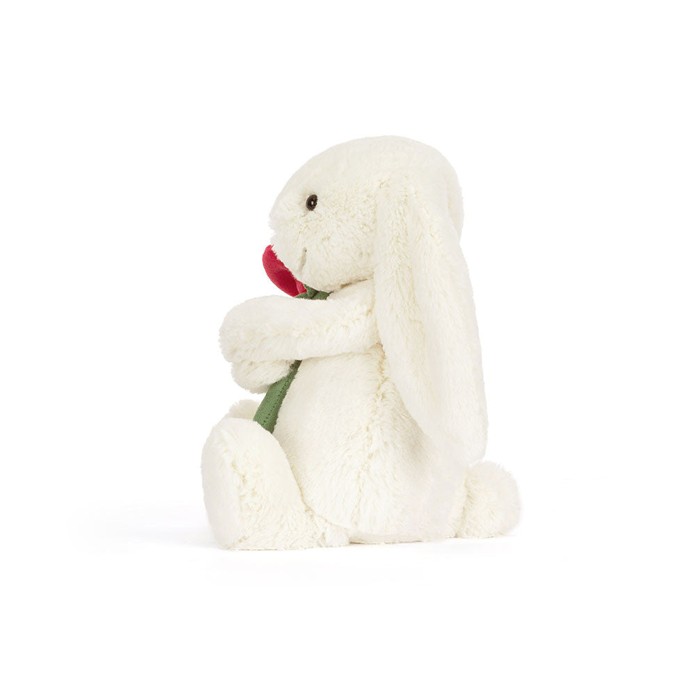 side view of White plush bunny holding a red rose on a white background