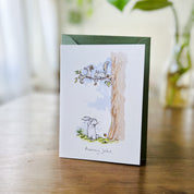 greeting card standing on wood table with an illustration of squirrels throwing acorns at bunny from tree, text reads 'acorny joke'