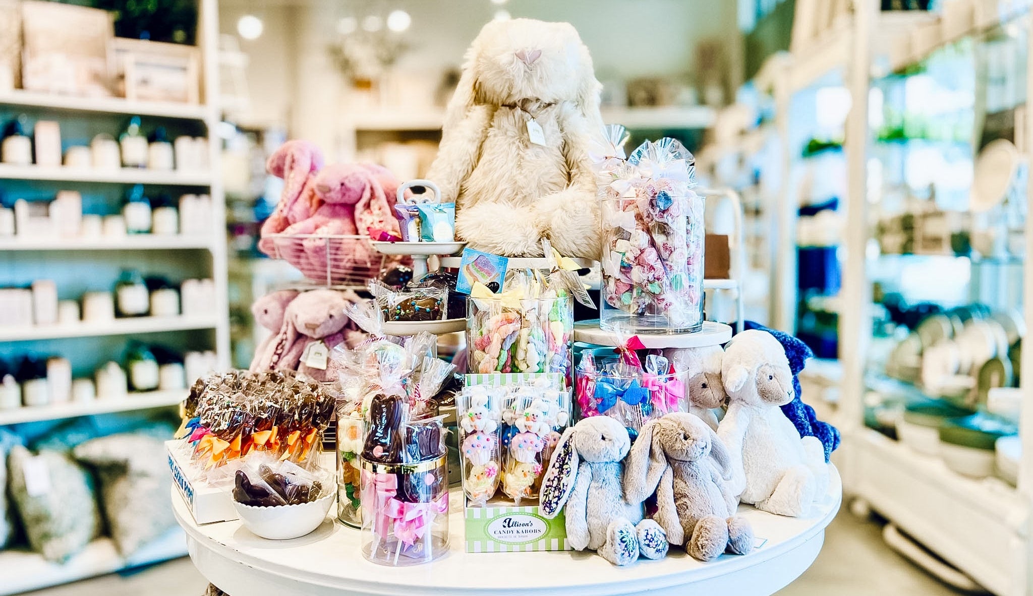 Display of plush toy bunnies and lambs, along with easter candy with a blurred background showing more decor shelving in a store setting