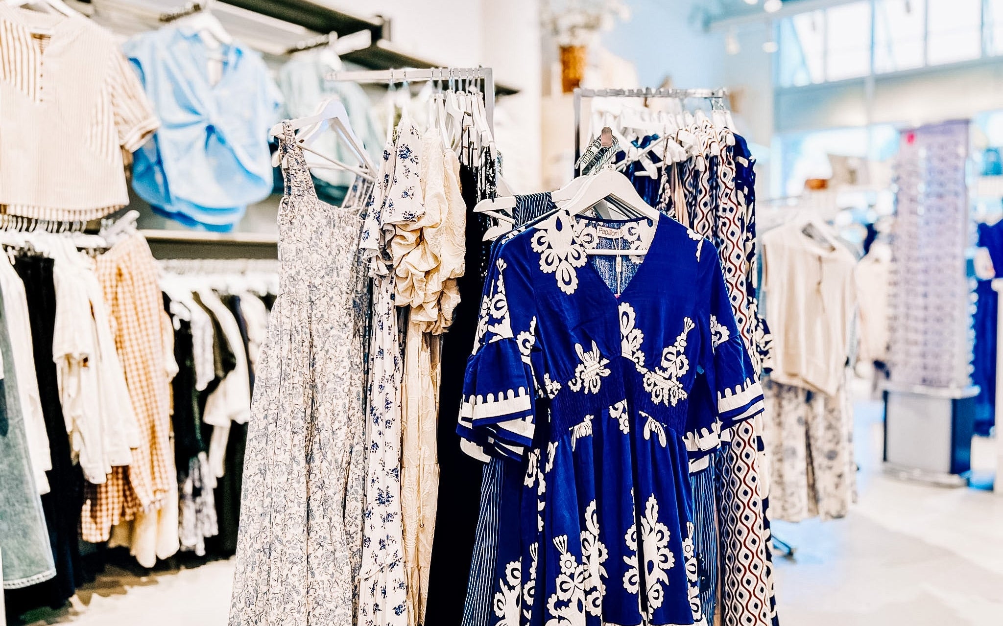 Blue dress with white patterns on a rack in a clothing store with other styled around and behind