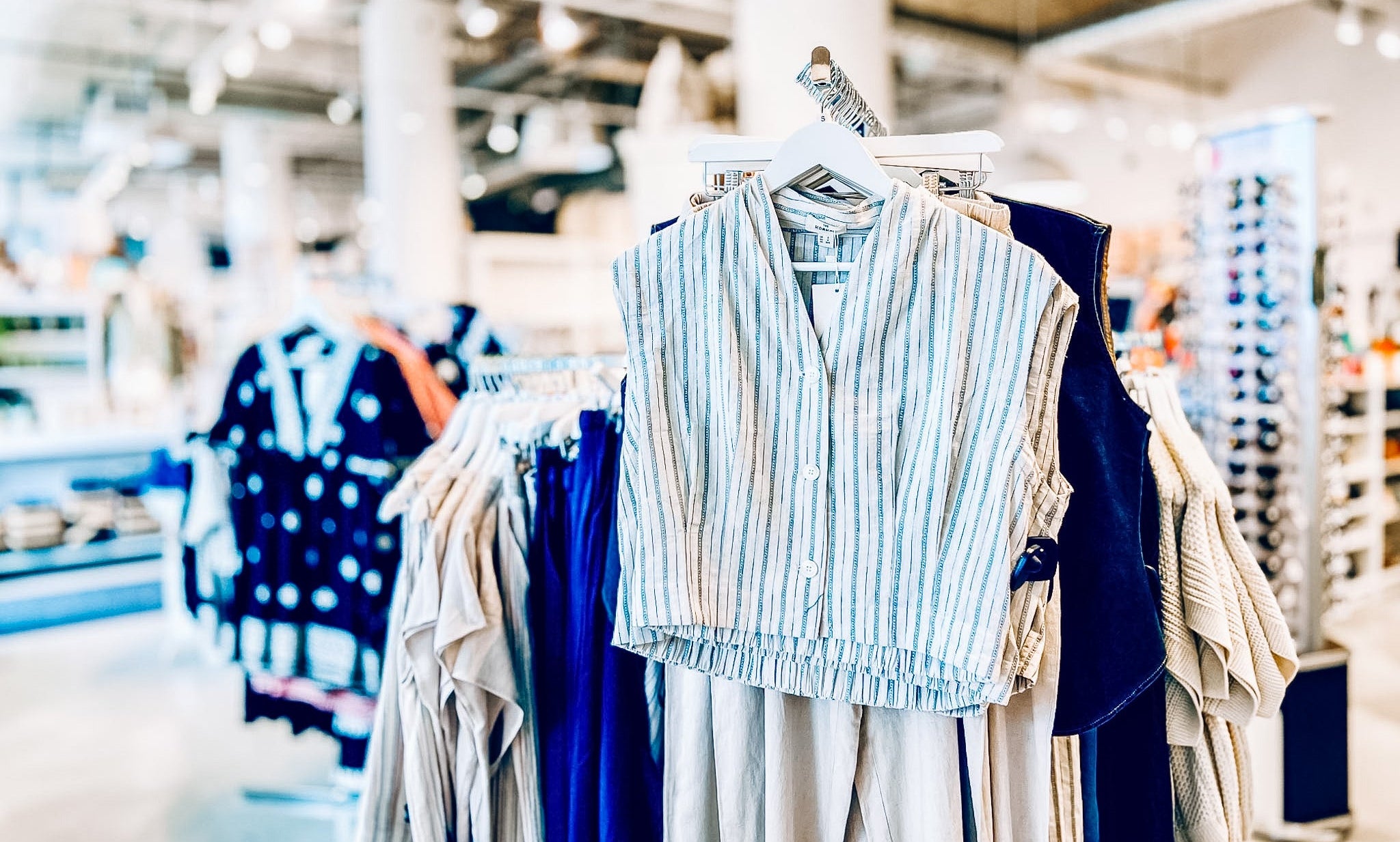 Clothing rack with striped shirt and pants in a store setting with blurred background showing more fashion and sunglasses