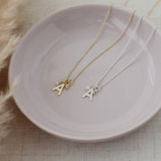 Two delicate initial necklaces with letter 'A' pendants, one in gold and one in silver, displayed on a light pink ceramic plate.