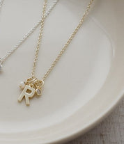 A delicate gold initial necklace with an 'R' charm and a small matching charm, displayed on a light beige ceramic plate.