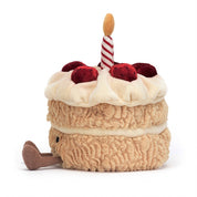 side view of fluffy stuffed plush toy of vanilla birthday cake with red berries, white frosting, candle and black smiley face