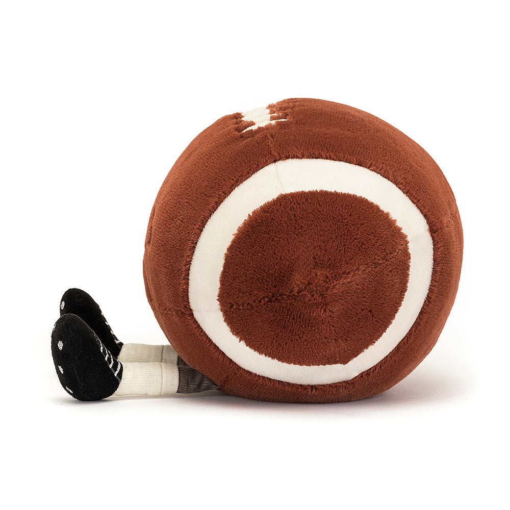 side view of fuzzy soft brown american football stuffed plush toy with black smiley face and cleats made by jellycat