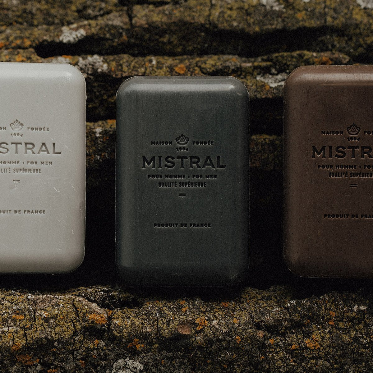Three bars of Mistral soap in different colors against a textured stone background
