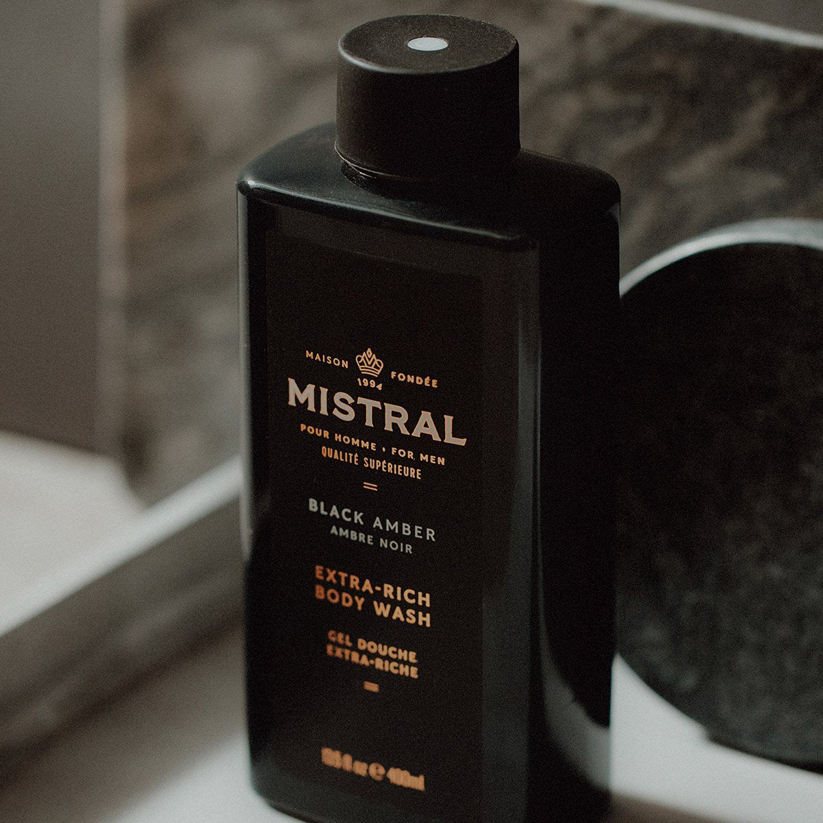 Black bottle of Mistral Black Amber Extra-Rich Body Wash on a bathroom counter.
