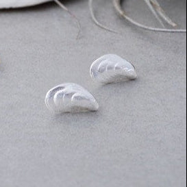 Pair of gold and silver MUSSEL SHELL-shaped earrings on a light gray surface with seashells in the background.