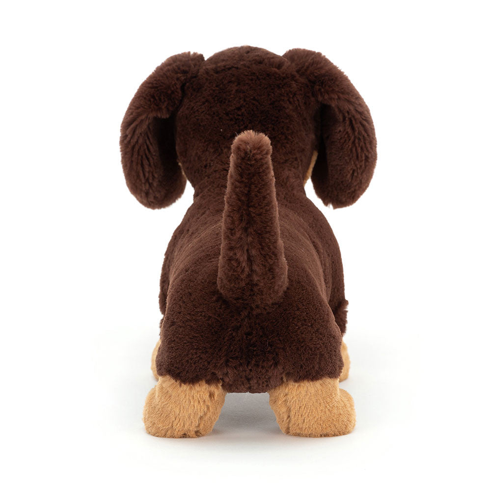 Back view of plush sausage dog toy with dark brown fur and beige feet on a white background. 