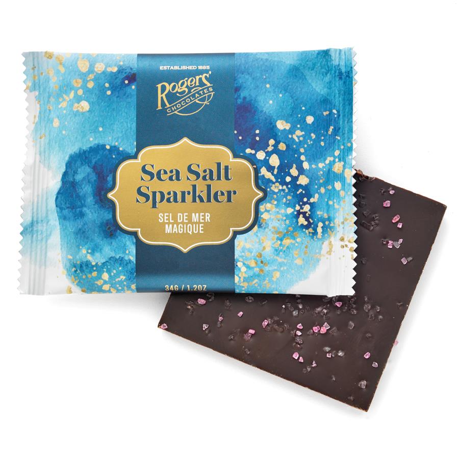 sea sparkler chocolate bar by roger's. Package is bright blue with gold and white. Under is square dark chocolate bar with pink sea salt on top. 