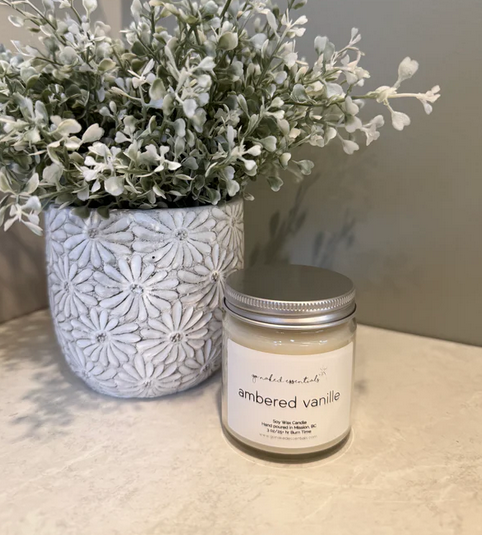Candle labeled 'ambered vanille' next to a decorative plant on a textured surface.