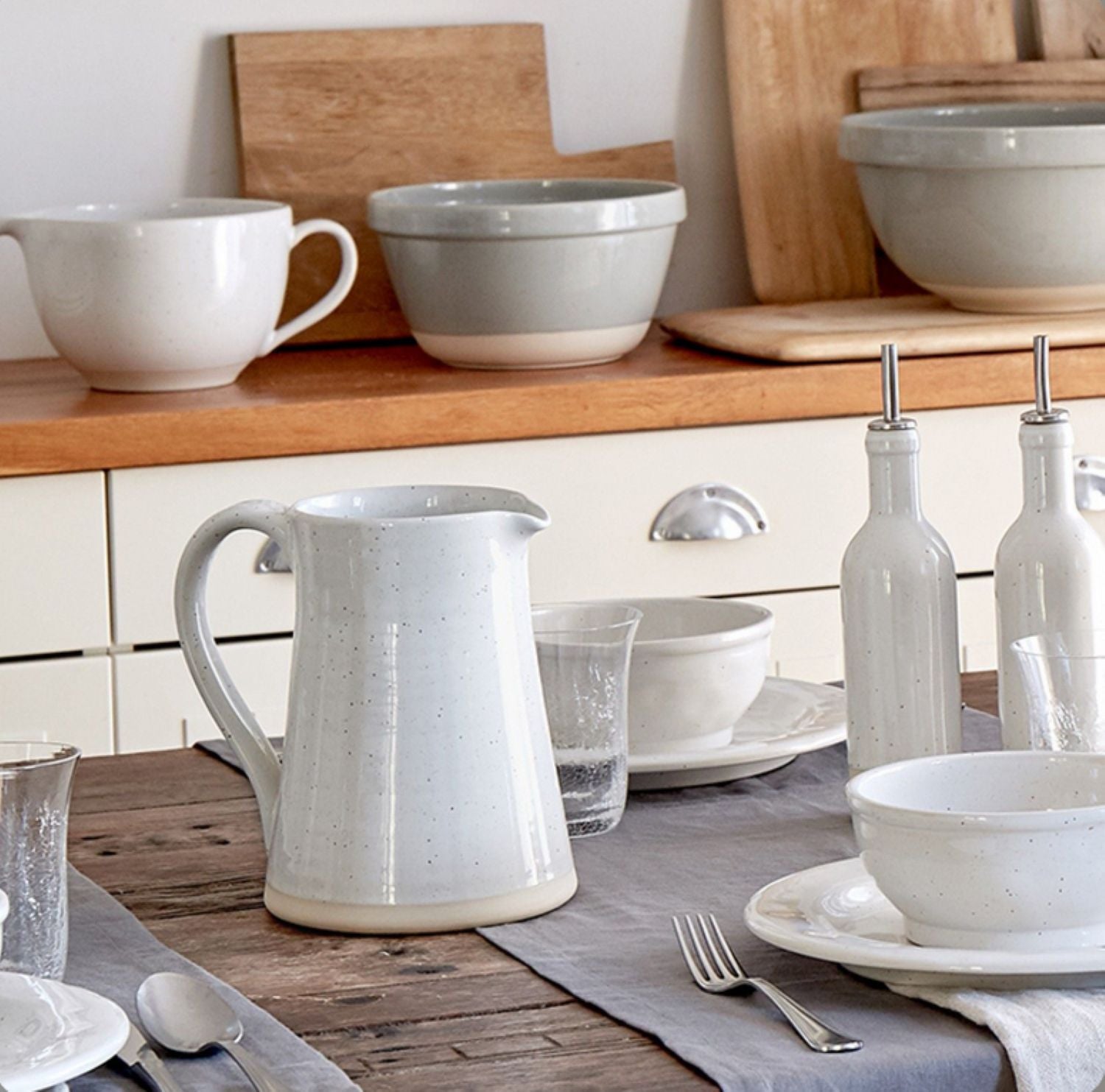Ceramic tableware including bowls, cups, and a pitcher on a wooden table.