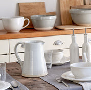 Ceramic tableware including bowls, cups, and a pitcher on a wooden table.