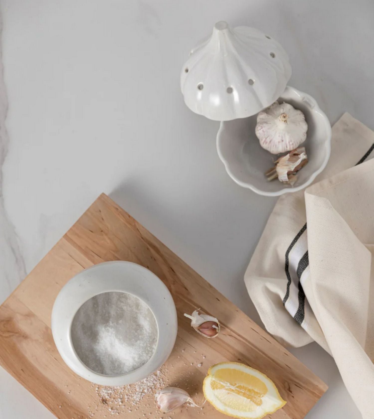 White ceramic salt shaker on a wooden cutting board with a lemon and garlic cloves.
