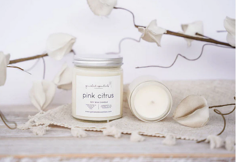 Candle labeled 'pink citrus' on a decorative surface with white flowers and branches.